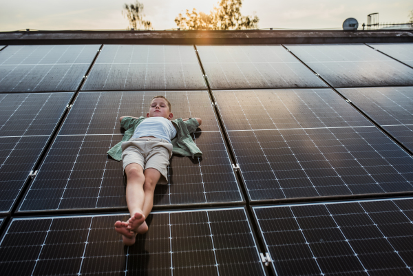 Boy lying on roof with solar panels, eyes closed. Sustainable future for next generation concept.