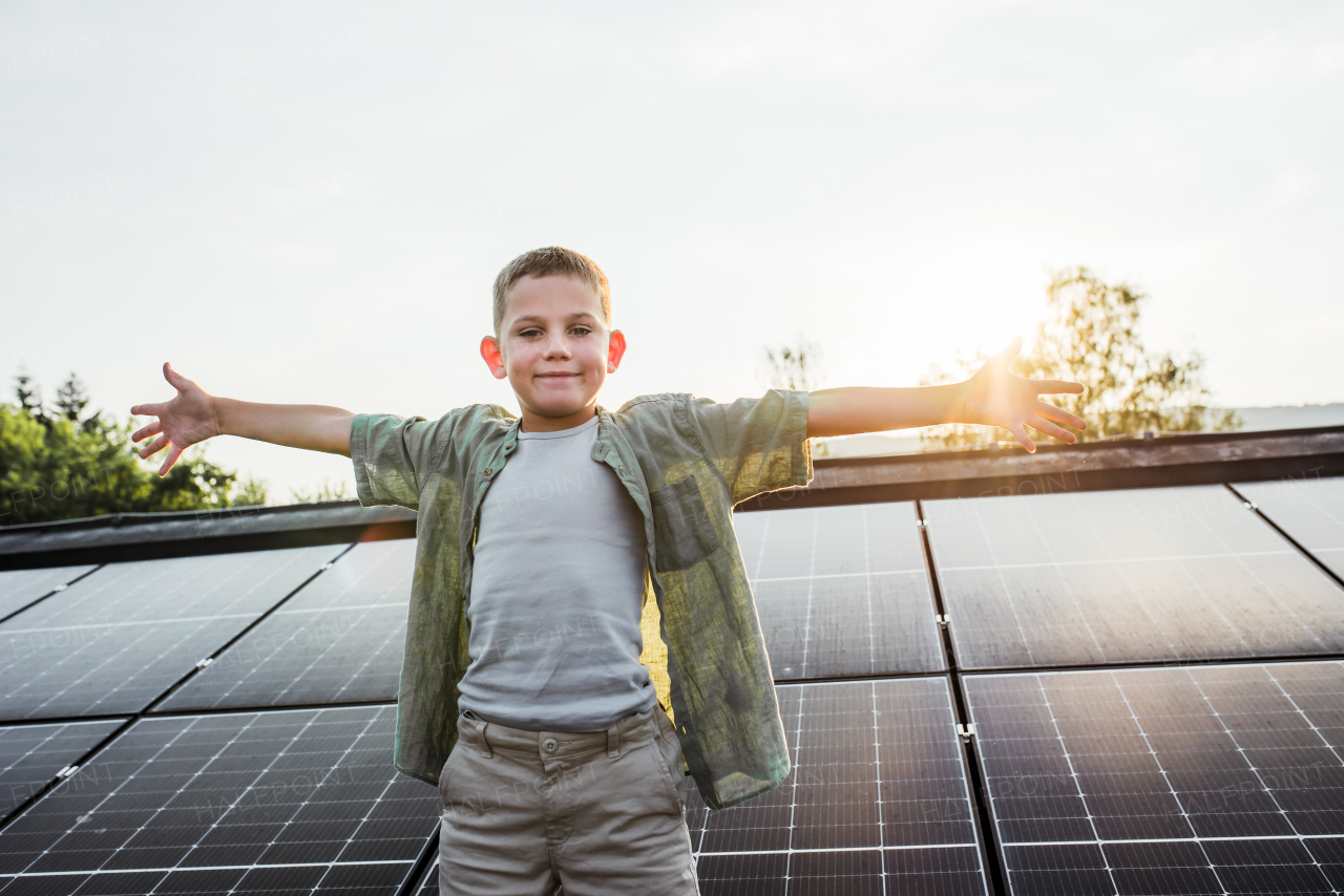 Cute boy standing on roof with solar panels with open arms. Rooftop solar or photovoltaic system. Sustainable future for next generation concept.