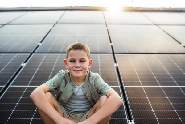 Cute boy sitting on roof with solar panels, looking at camera. Sustainable future for next generation concept.