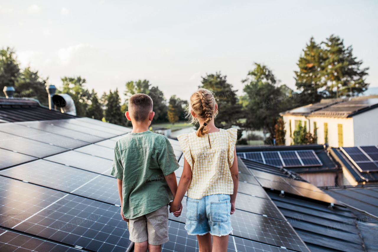 Two young siblings on roof with solar panels, holding each other.Sustainable future for next generation concept.