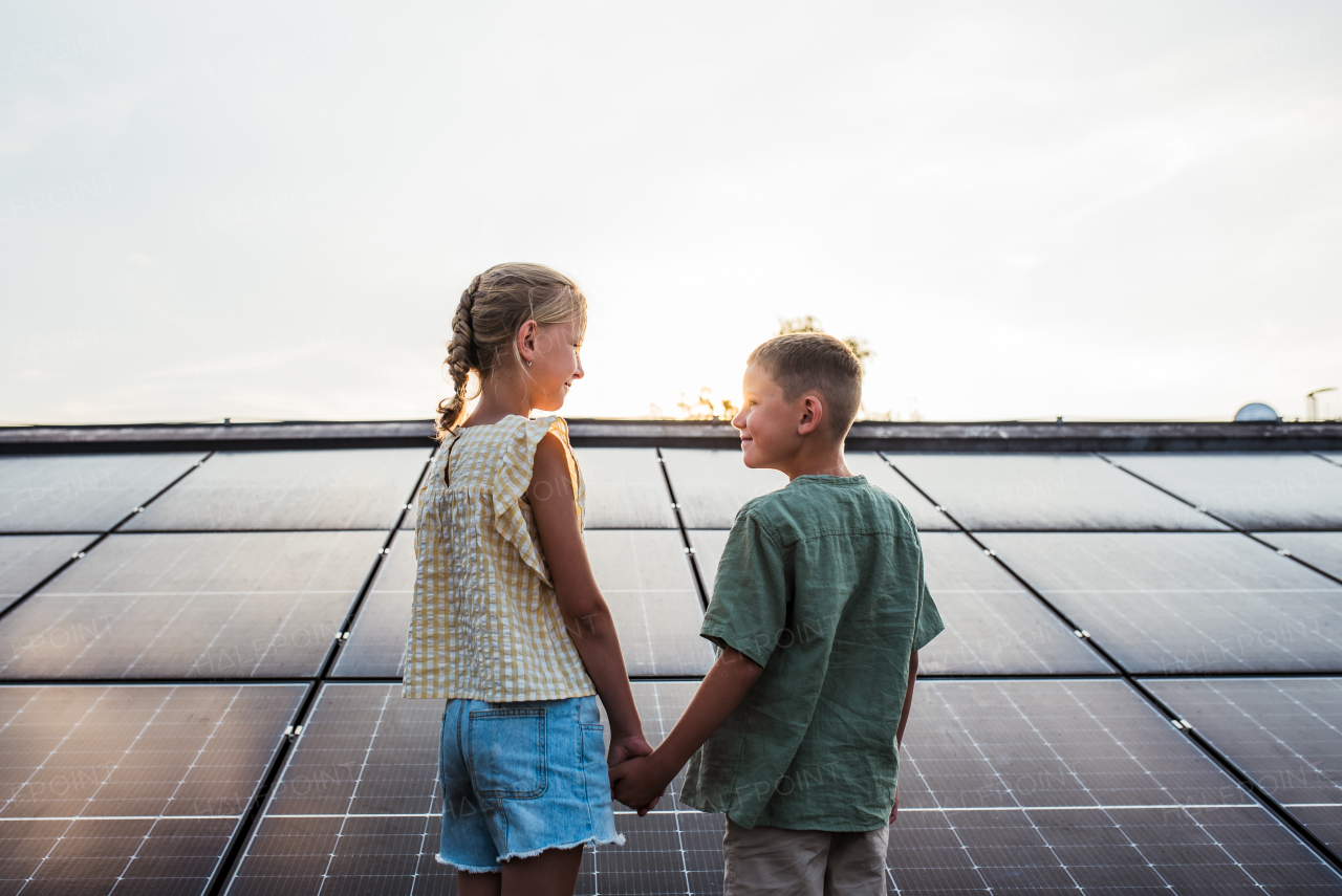 Two young siblings on roof with solar panels, looking at each other.Sustainable future for next generation concept.