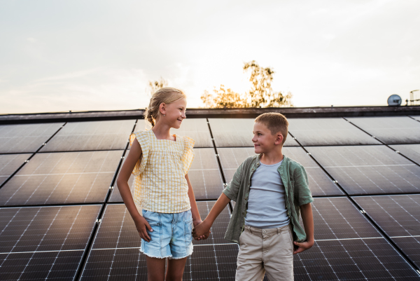 Two young siblings on roof with solar panels, looking at each other.Sustainable future for next generation concept.