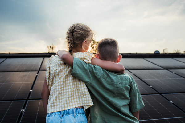 Two young siblings on roof with solar panels, holding each other.Sustainable future for next generation concept.