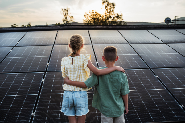 Two young siblings on roof with solar panels, holding each other.Sustainable future for next generation concept.