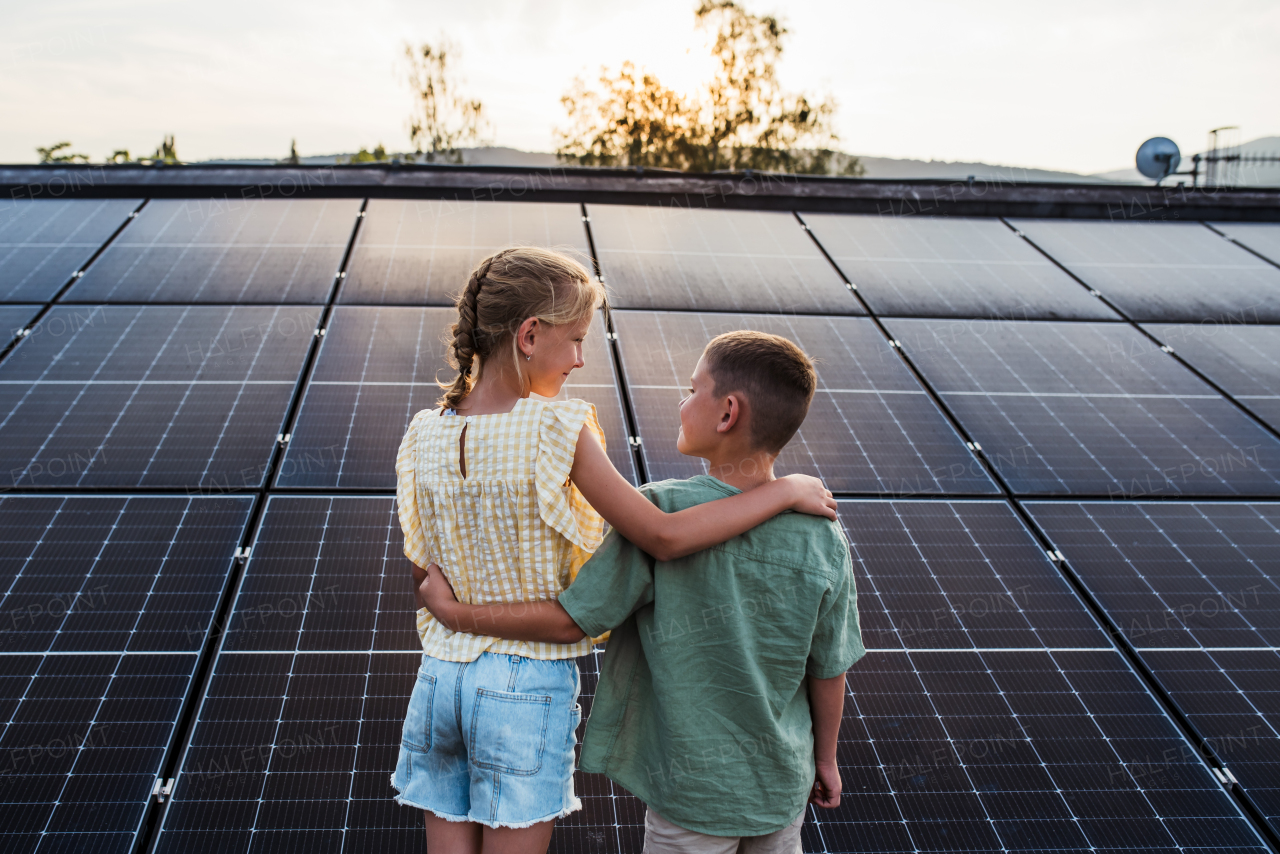 Two young siblings on roof with solar panels, holding each other.Sustainable future for next generation concept.