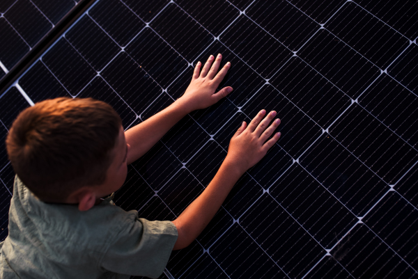 Boy lying on belly on roof with solar panels, touching panel with hands. Sustainable future for next generation concept.