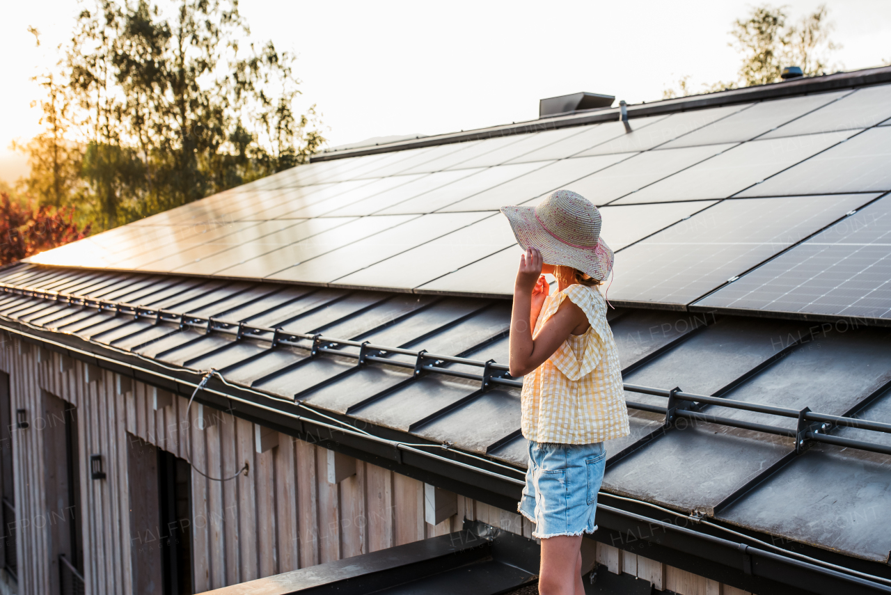 Girl standing in front of roof with solar panels during sunset, holding her hat. Sustainable future for next generation concept.