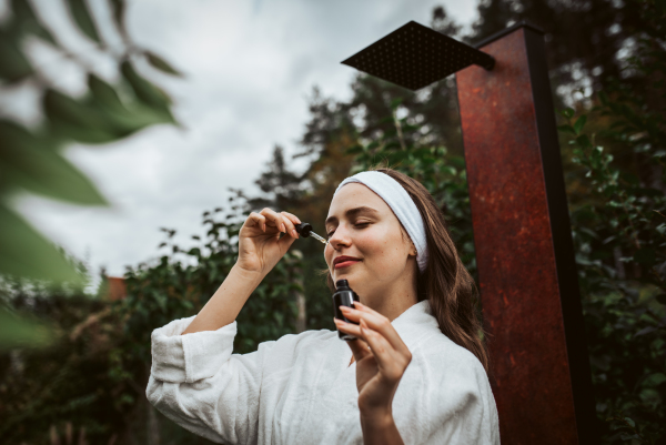 Beautiful woman doing her skin care routine outdoors, wearing bathrobe. Woman using facial skin serum