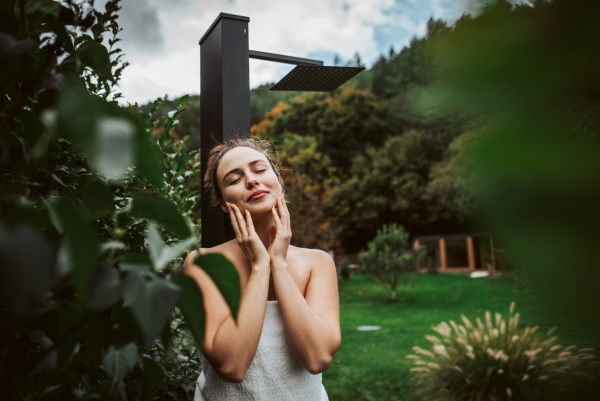 Beautiful woman touching her face, stainding outdoor in the garden. Woman taking care of her body and mind, wellness routine