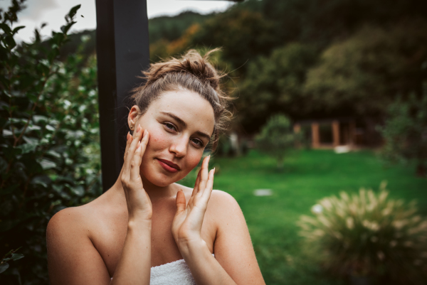 Beautiful woman touching her face, stainding outdoor in the garden. Woman taking care of her body and mind, wellness routine