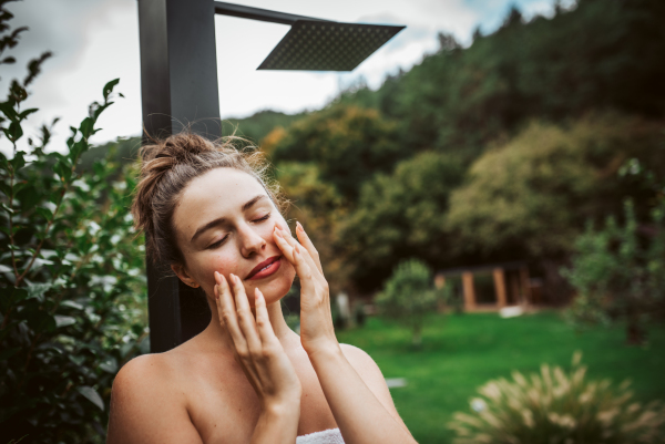 Beautiful woman touching her face, stainding outdoor in the garden. Woman taking care of her body and mind, wellness routine