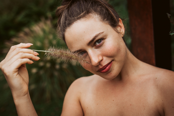 Portrait of a beautiful woman standing in a garden, holding a ornamental grass in her hand. Mental well-being and connection with nature