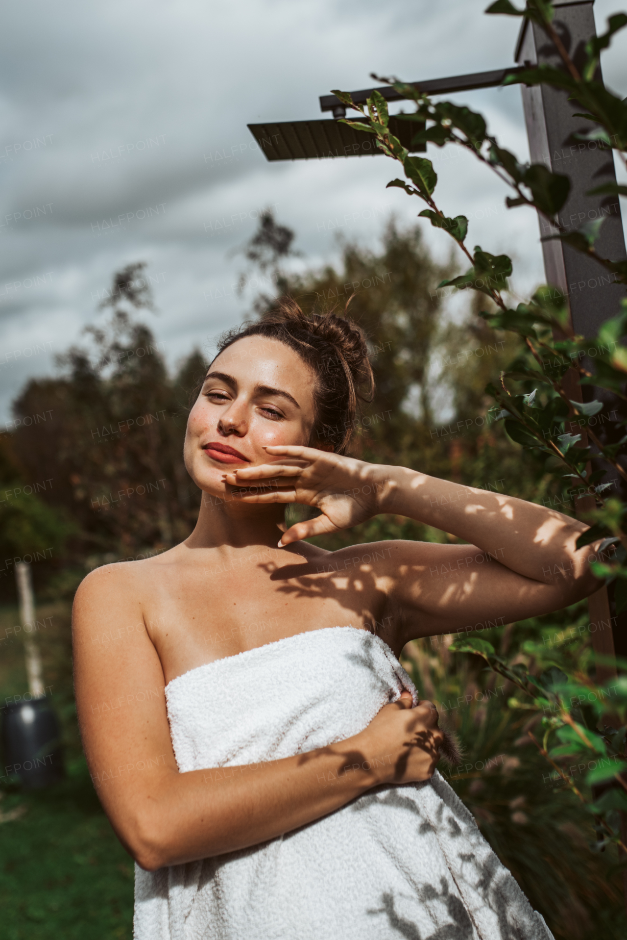 Beautiful woman touching her face, stainding outdoor in the garden. Woman taking care of her body and mind, wellness routine