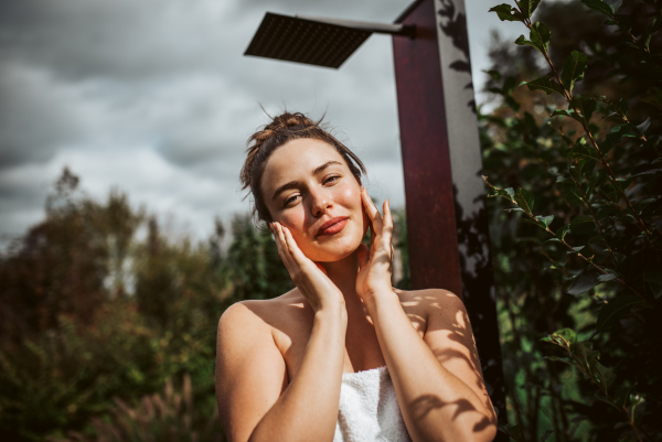 Beautiful woman touching her face, stainding outdoor in the garden. Woman taking care of her body and mind, wellness routine