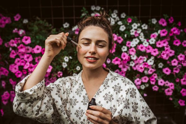 Beautiful woman doing her skin care routine outdoors, wearing bathrobe. Woman using facial skin serum