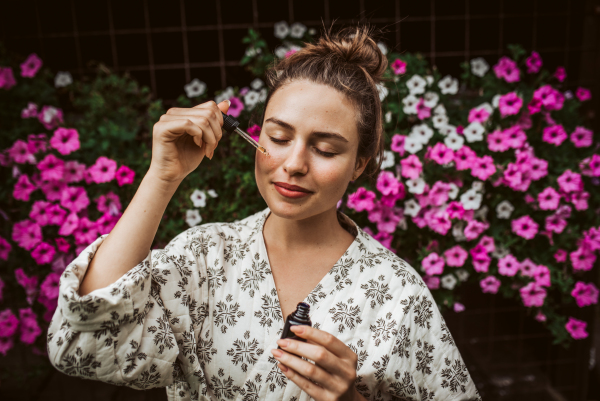 Beautiful woman doing her skin care routine outdoors, wearing bathrobe. Woman using facial skin serum