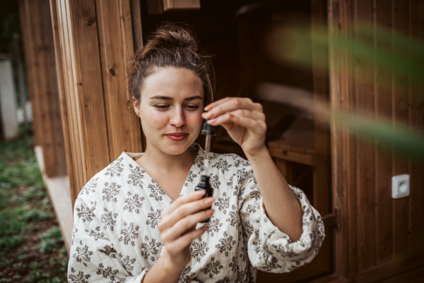 Beautiful woman doing her skin care routine outdoors, wearing bathrobe. Woman using facial skin serum