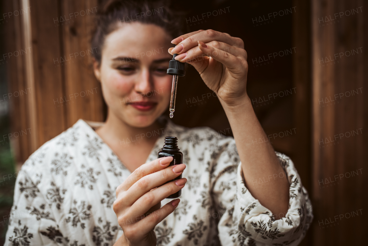 Beautiful woman doing her skin care routine outdoors, wearing bathrobe. Woman using facial skin serum