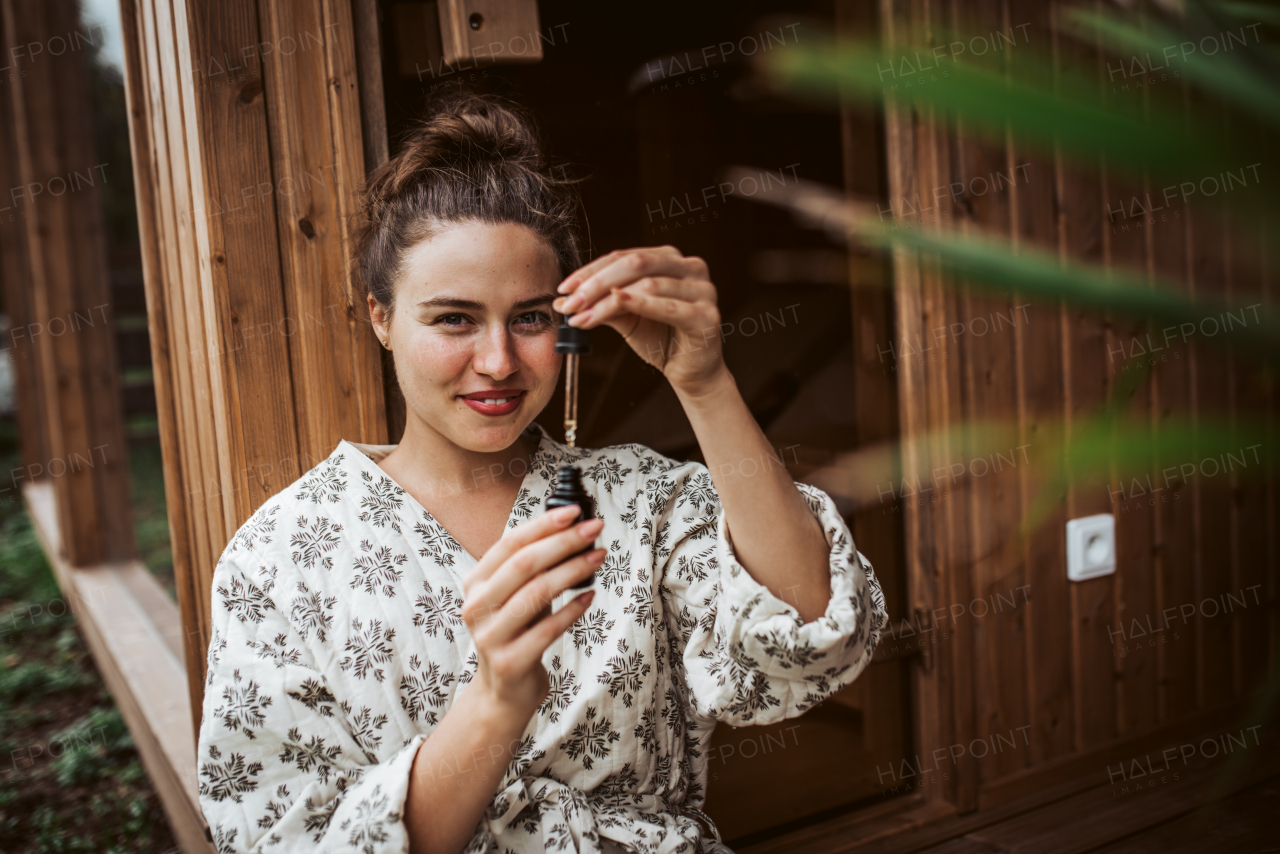 Beautiful woman doing her skin care routine outdoors, wearing bathrobe. Woman using facial skin serum