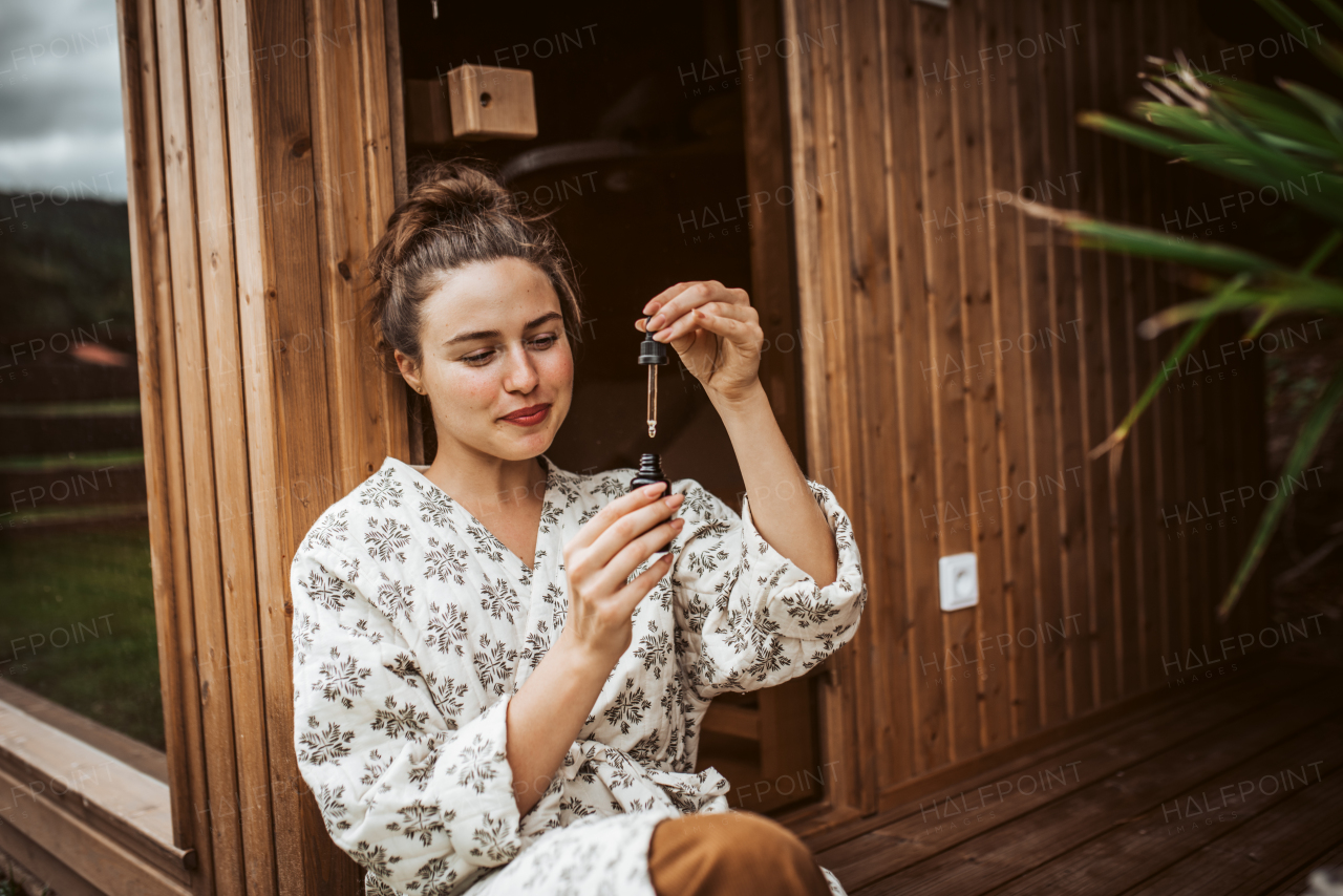 Beautiful woman doing her skin care routine outdoors, wearing bathrobe. Woman using facial skin serum