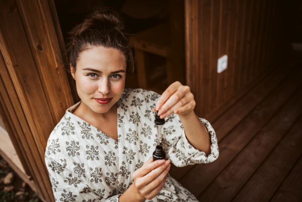 Beautiful woman doing her skin care routine outdoors, wearing bathrobe. Woman using facial skin serum