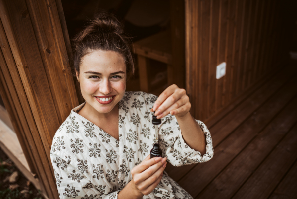 Beautiful woman doing her skin care routine outdoors, wearing bathrobe. Woman using facial skin serum