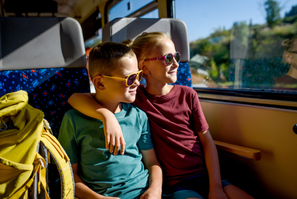 Siblings sitting in train, looking out of window. Family going on hike, using a public transport.