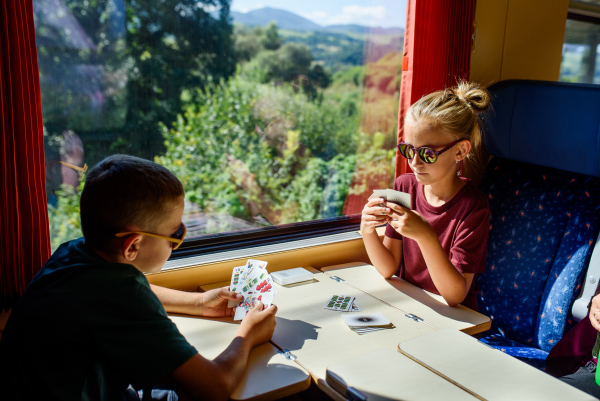 Siblings sitting in train, playing cards, having fun. Family going on hike, using a public transport.