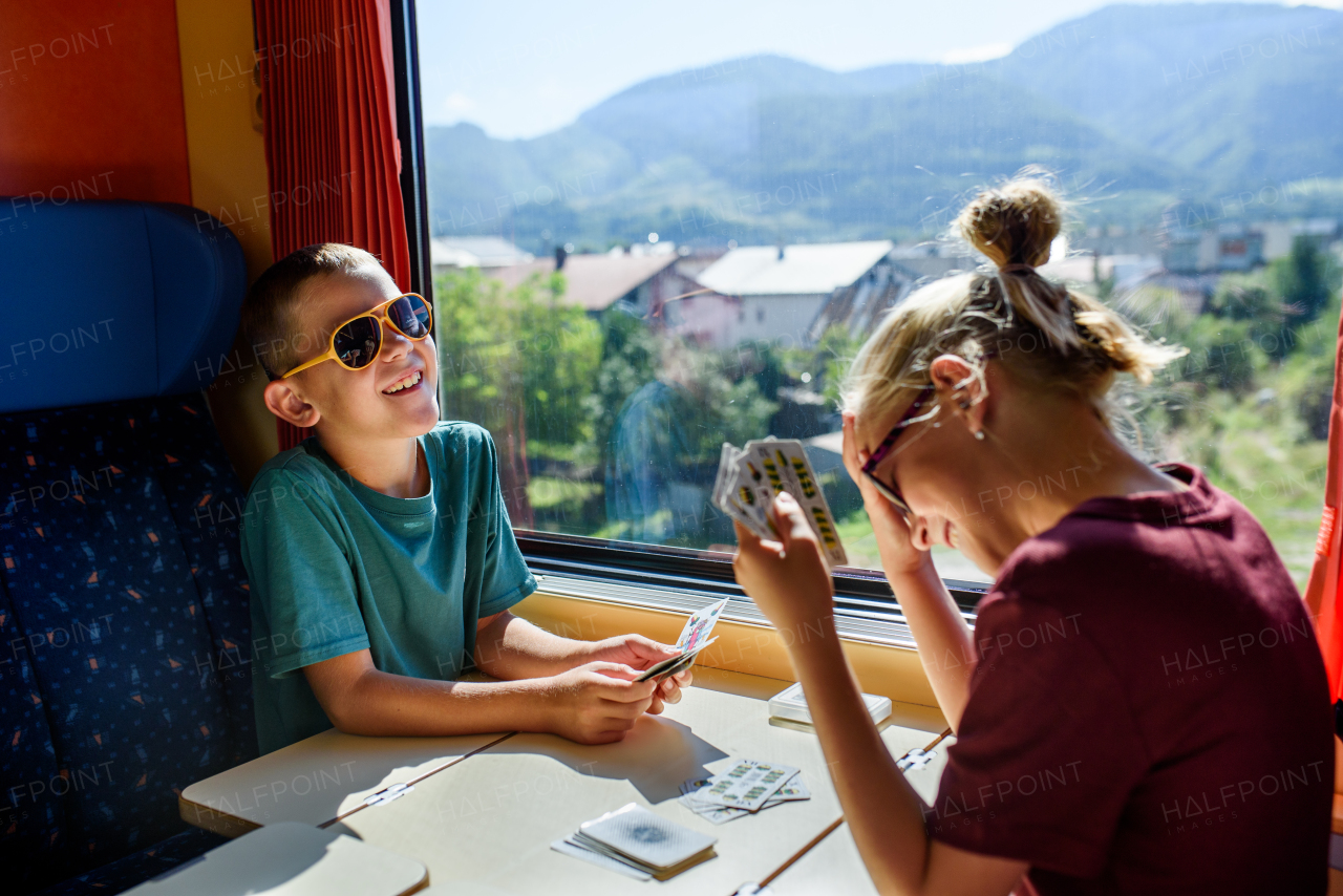 Siblings sitting in train, playing cards, having fun. Family going on hike, using a public transport.