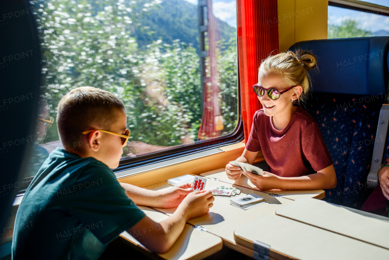 Siblings sitting in train, playing cards, having fun. Family going on hike, using a public transport.