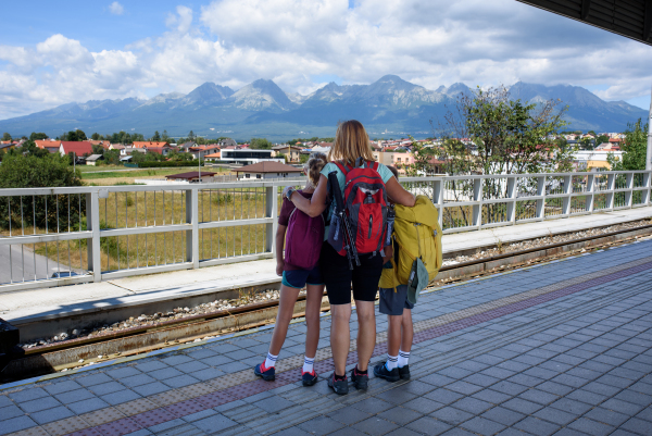 Grandma with grandchildren waiting for train, standing on the platform. Family going on hike, using public transport.