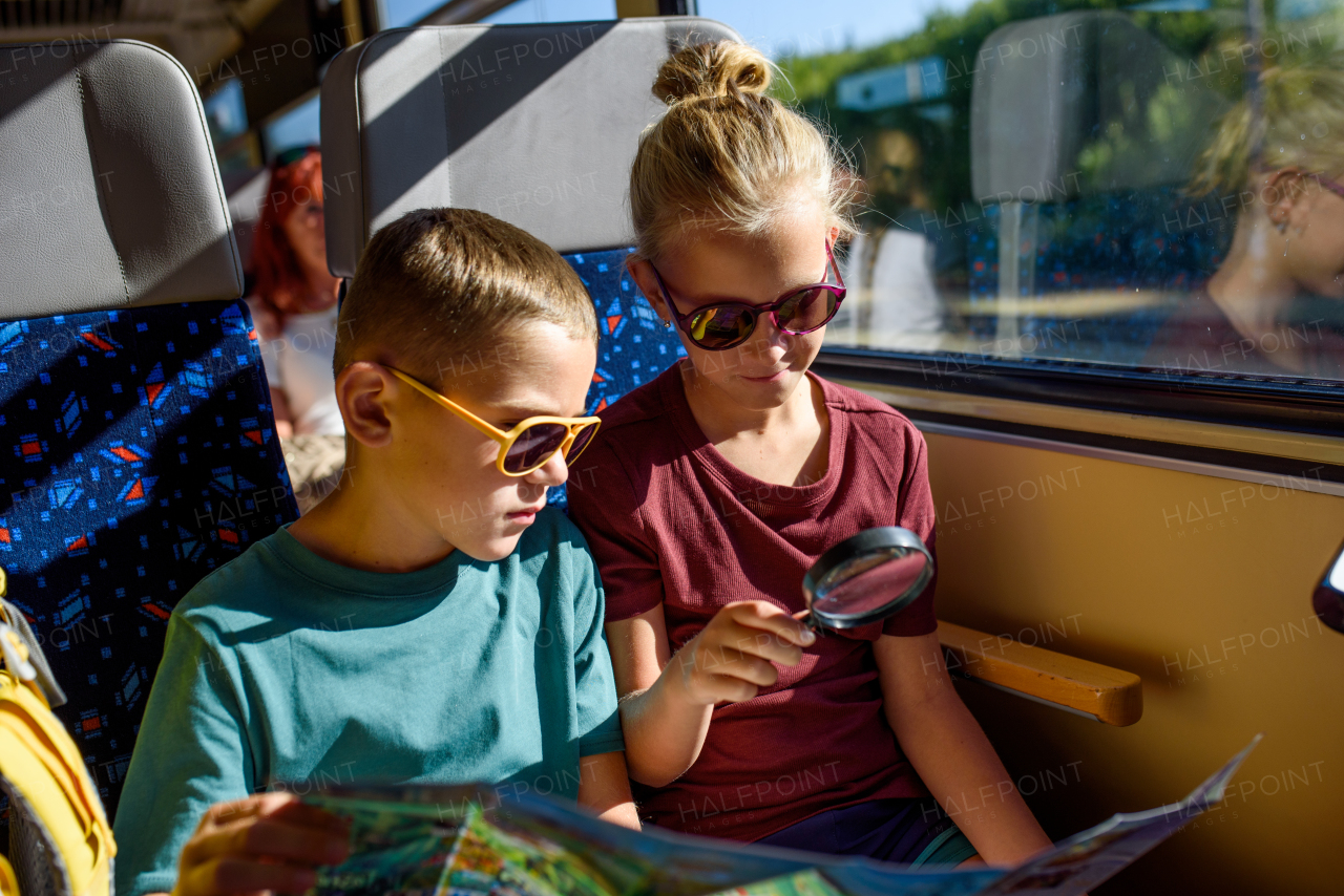 Siblings sitting in train, looking at map with magnifying glass. Family going on hike, using a public transport.