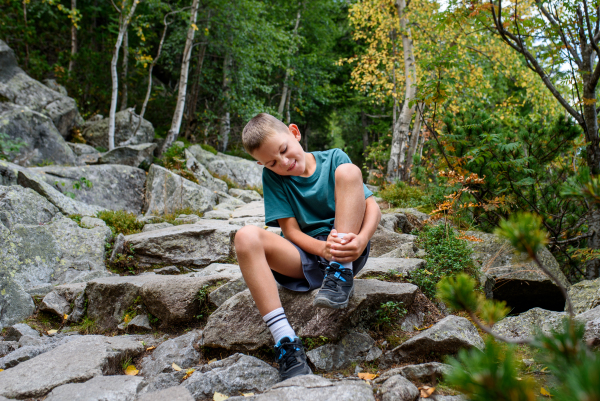 Boy with injury on hike in autumn mountains. Kid fell, feeling pain in his ankle.