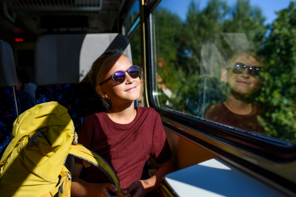 Girl sitting in train, looking out of window and enjoying journey. Family going on hike, using a public transport.