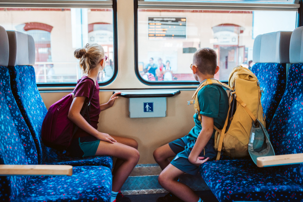 Siblings with backpacks sitting in train, looking out of window. Family going on hike, using a public transport.