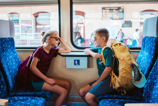 Siblings with backpacks sitting in train, looking at each other. Family going on hike, using a public transport.