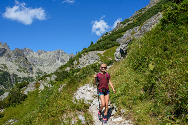 Cute girl walking down the hiking trail. Kids spending summer break in nature with a family.