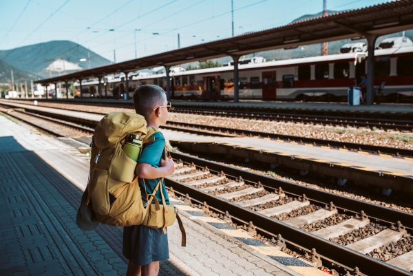 Boy waiting for train, standing on the platform. Family going on hike, using public transport.