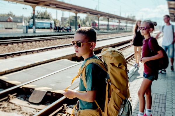 Siblings waiting for train, standing on the platform. Family going on hike, using public transport.