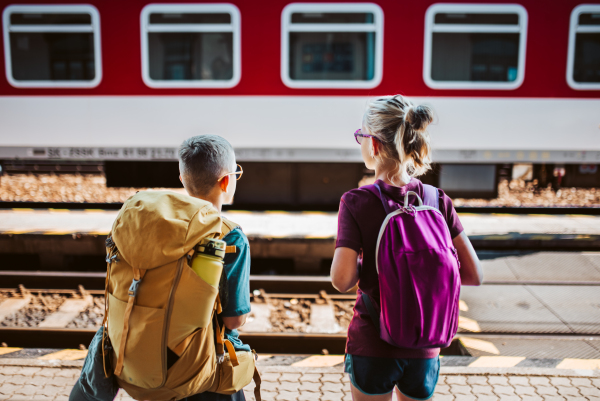 Siblings waiting for train, standing on the platform. Family going on hike, using public transport.