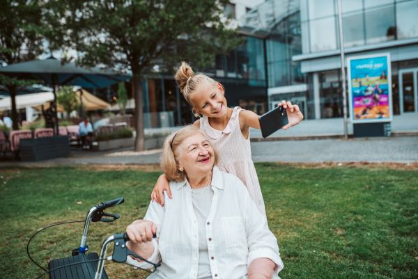 Grandma taking selfie with granddaugter sitting on bench. Girl spending time with senior grandmother, during summer break or after school.