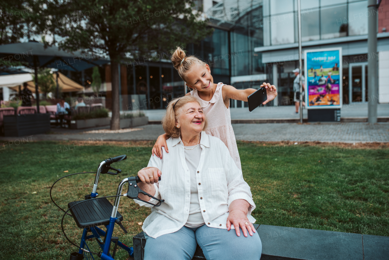 Grandma taking selfie with granddaugter sitting on bench. Girl spending time with senior grandmother, during summer break or after school.