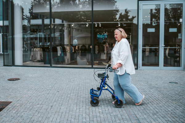 Senior woman walking on city street with rollator, running errands.