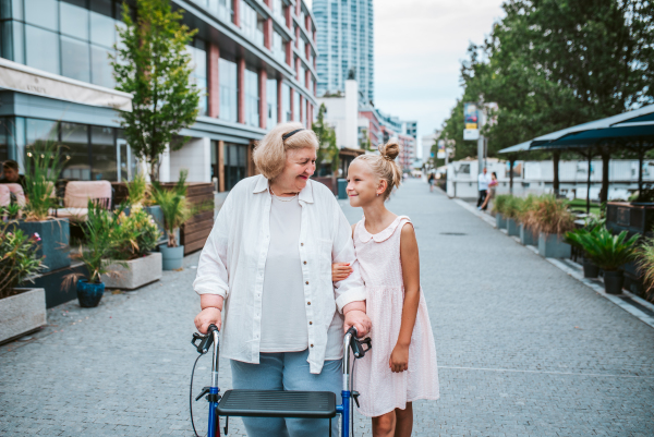 Grandma with walker and granddaugter in the city, on walk. Girl spending time with senior grandmother, during holidays, after school.