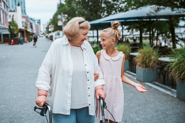 Grandma with walker and granddaugter in the city, on walk. Girl spending time with senior grandmother, during holidays, after school.