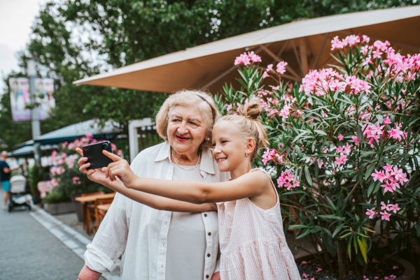 Grandma taking selfie with granddaugter standing on the street. Girl spending time with senior grandmother, during summer break or after school.