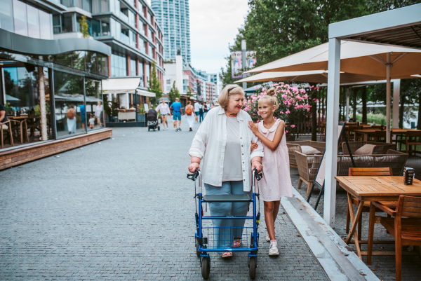 Grandma with walker and granddaugter in the city, on walk. Girl spending time with senior grandmother, during holidays, after school.