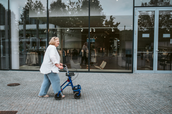 Senior woman walking on city street with rollator, running errands.