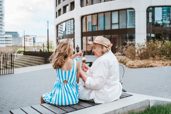 Grandma and granddaugter in the city, sitting on bench. Girl spending time with senior grandmother, during holidays, after school.