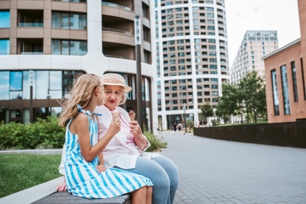 Grandma and granddaugter in the city, sitting on bench. Girl spending time with senior grandmother, during holidays, after school.